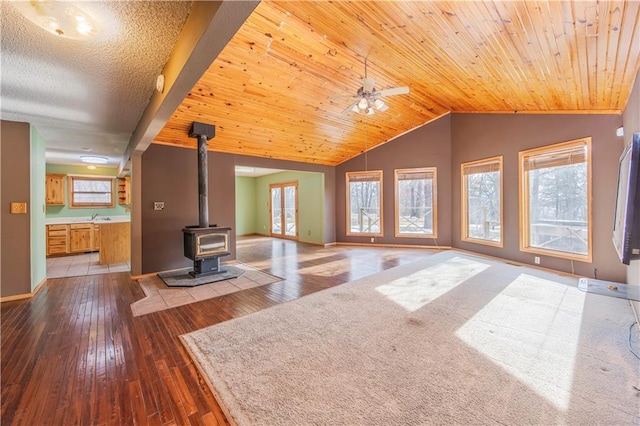 unfurnished living room featuring ceiling fan, a wood stove, wood-type flooring, and wood ceiling