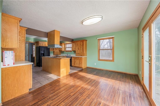 kitchen with light hardwood / wood-style floors, a textured ceiling, a center island, and black fridge with ice dispenser