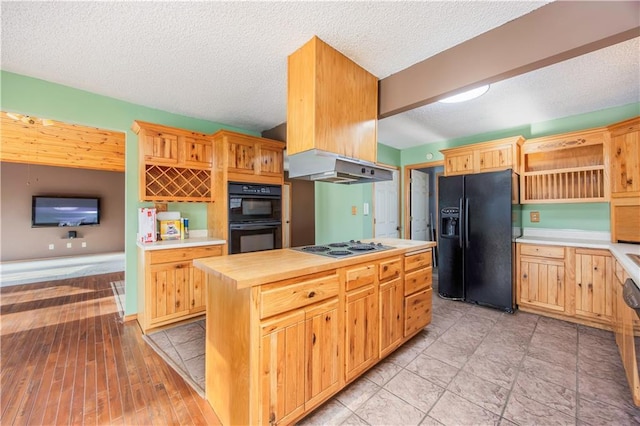 kitchen featuring a textured ceiling, butcher block counters, a center island, and black appliances