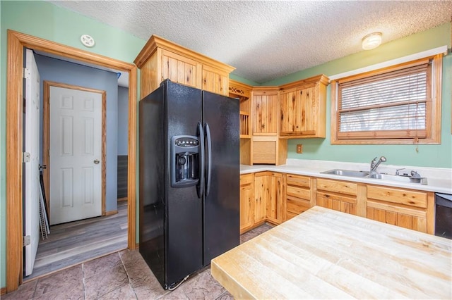 kitchen with black refrigerator with ice dispenser, sink, a textured ceiling, and light brown cabinets