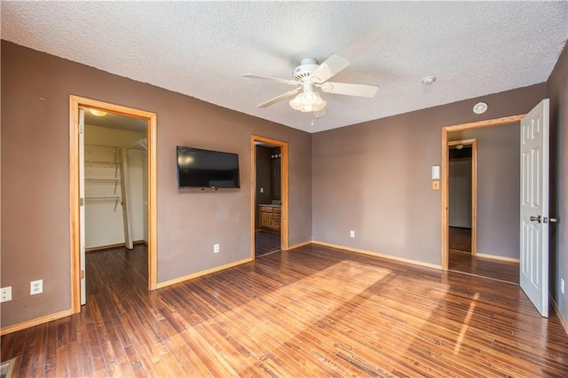 unfurnished bedroom featuring ceiling fan, connected bathroom, a closet, wood-type flooring, and a walk in closet