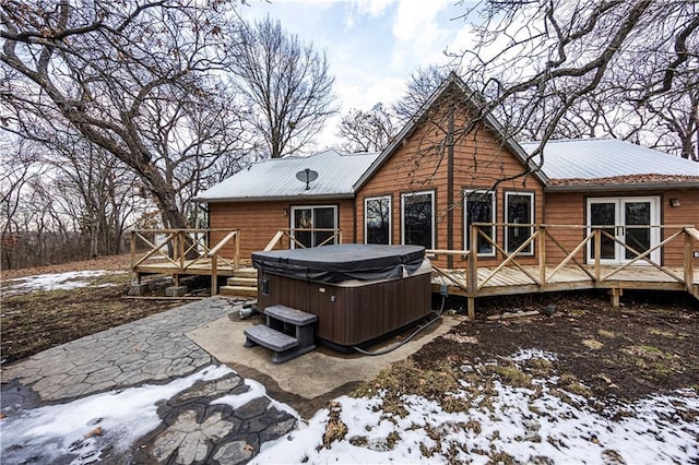 snow covered rear of property with a deck, a patio area, and a hot tub