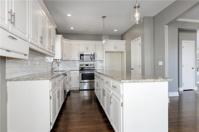 kitchen featuring sink, appliances with stainless steel finishes, white cabinetry, light stone countertops, and a kitchen island