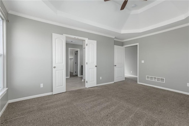 unfurnished bedroom featuring multiple windows, ornamental molding, a raised ceiling, and carpet flooring