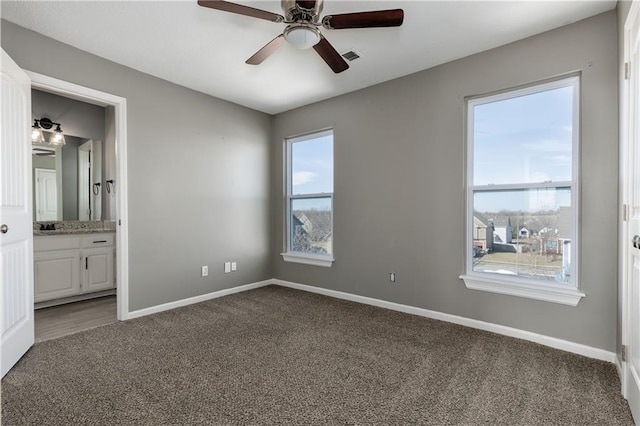 unfurnished bedroom with ceiling fan, ensuite bath, and dark carpet