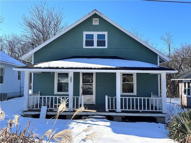 snow covered back of property with covered porch and central AC unit