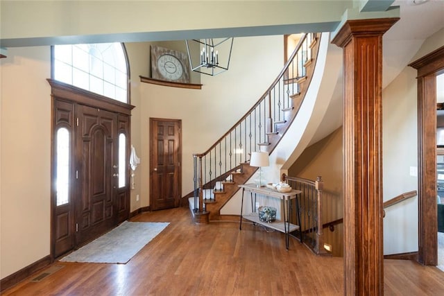 foyer featuring a towering ceiling, ornate columns, stairway, and wood finished floors