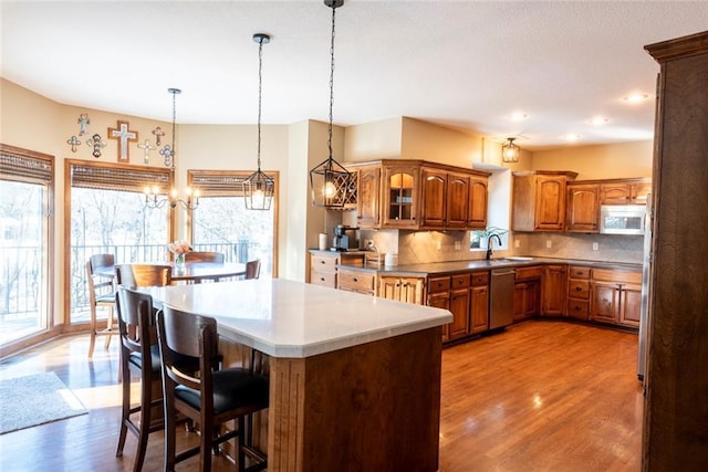 kitchen with brown cabinetry, decorative backsplash, white microwave, a kitchen island, and light wood-type flooring