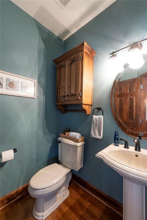 half bathroom featuring a sink, wood finished floors, toilet, and baseboards