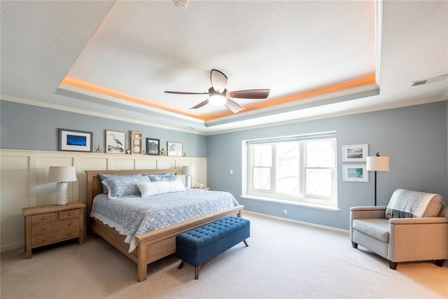 bedroom with ornamental molding, a tray ceiling, visible vents, and light colored carpet