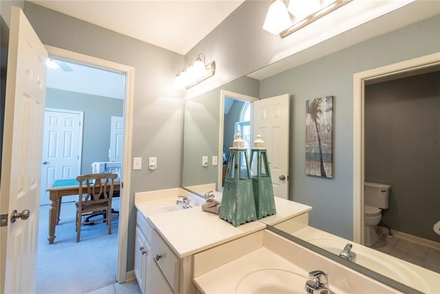 bathroom with baseboards, a sink, toilet, and double vanity