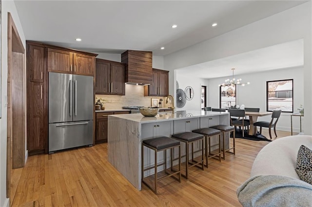 kitchen with pendant lighting, stainless steel fridge, a breakfast bar area, a kitchen island with sink, and light hardwood / wood-style floors