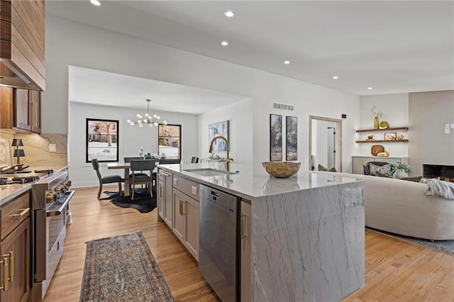 kitchen featuring a large island, sink, appliances with stainless steel finishes, light stone countertops, and decorative light fixtures