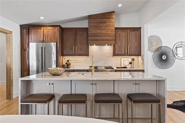 kitchen with an island with sink, high end refrigerator, light hardwood / wood-style floors, and vaulted ceiling