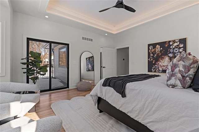 bedroom with a raised ceiling, light wood-type flooring, access to exterior, and ceiling fan