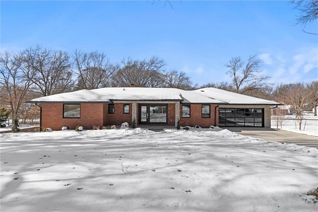 snow covered house with brick siding, driveway, and a garage