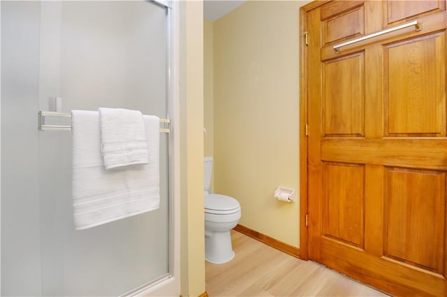 bathroom featuring hardwood / wood-style flooring, a shower with door, and toilet