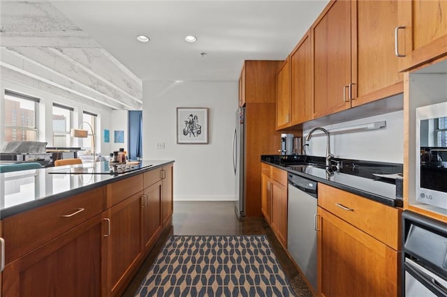 kitchen with recessed lighting, stainless steel appliances, a sink, brown cabinetry, and dark countertops