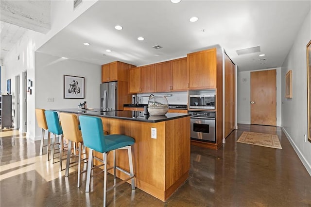 kitchen with visible vents, a breakfast bar area, appliances with stainless steel finishes, brown cabinets, and concrete flooring