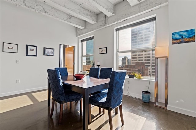 dining space featuring a healthy amount of sunlight, baseboards, concrete flooring, and beamed ceiling