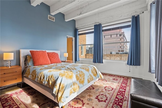 bedroom featuring baseboards, visible vents, beam ceiling, and wood finished floors