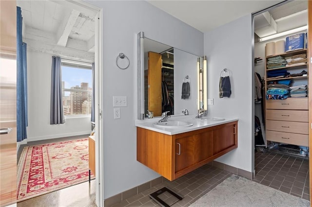 bathroom featuring double vanity, a sink, a walk in closet, and baseboards