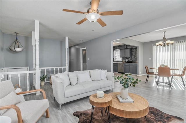 living room with ceiling fan with notable chandelier, light wood-type flooring, and sink