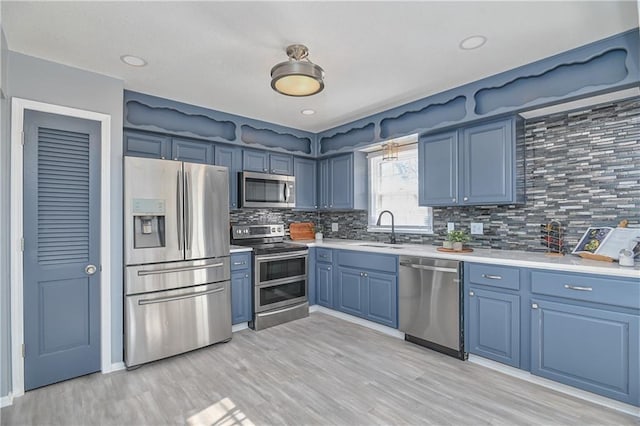 kitchen featuring appliances with stainless steel finishes, light wood-type flooring, blue cabinetry, decorative backsplash, and sink