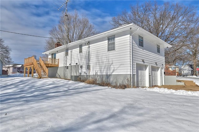 snow covered property featuring a garage and a wooden deck