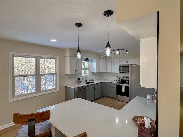 kitchen featuring sink, hanging light fixtures, gray cabinets, kitchen peninsula, and stainless steel appliances