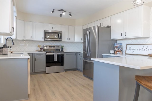 kitchen with sink, light hardwood / wood-style flooring, gray cabinets, a breakfast bar, and appliances with stainless steel finishes