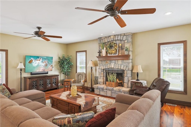 living room featuring ceiling fan, wood-type flooring, and a stone fireplace