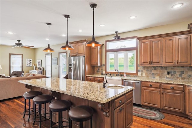 kitchen featuring stainless steel appliances, tasteful backsplash, hanging light fixtures, ceiling fan, and a center island with sink