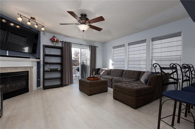 living room featuring ceiling fan, a textured ceiling, light hardwood / wood-style floors, and a fireplace