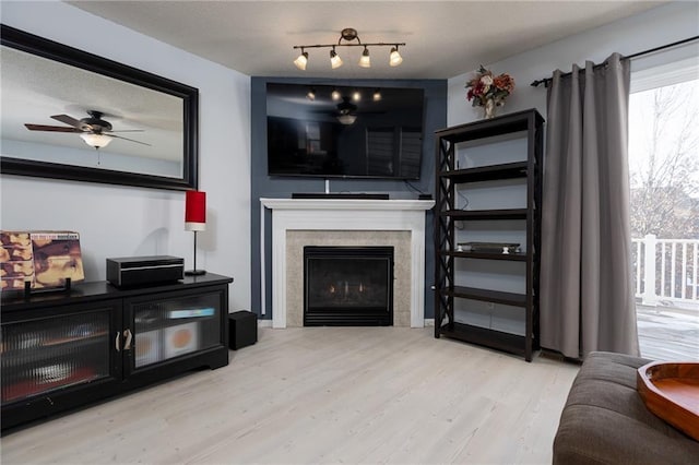 living room with ceiling fan, a tiled fireplace, a textured ceiling, and light wood-type flooring