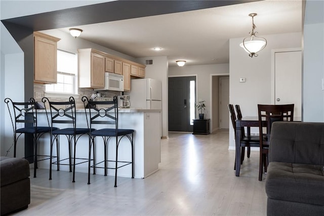 kitchen with light brown cabinetry, a breakfast bar area, light hardwood / wood-style floors, kitchen peninsula, and white appliances