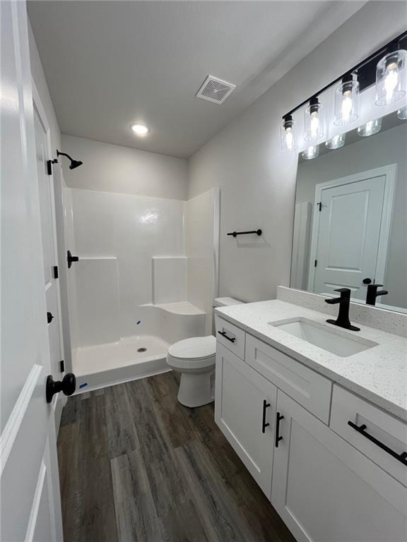 bathroom featuring a shower, hardwood / wood-style flooring, vanity, and toilet