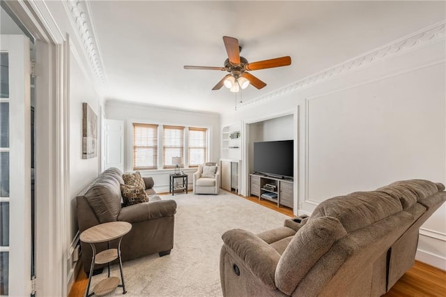 living room featuring ceiling fan, built in features, ornamental molding, and light hardwood / wood-style flooring