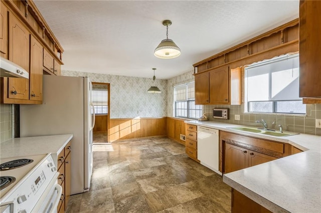 kitchen featuring sink, white appliances, hanging light fixtures, wooden walls, and decorative backsplash