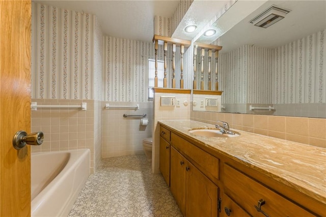 bathroom with vanity, tile walls, a bathtub, and toilet