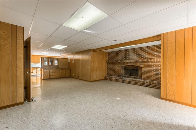 basement featuring wooden walls, a drop ceiling, and a fireplace