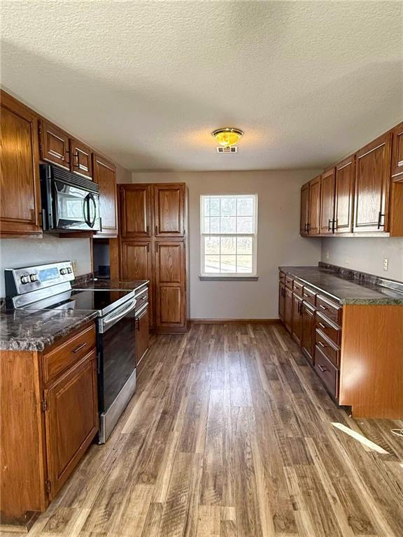 kitchen with dark wood-type flooring, a textured ceiling, and stainless steel range with electric stovetop