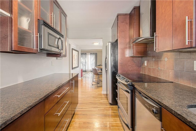 kitchen with stainless steel appliances, dark stone countertops, light wood-type flooring, decorative backsplash, and wall chimney range hood