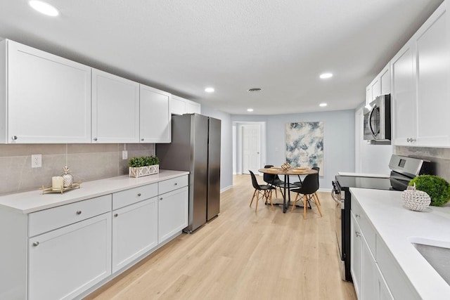 kitchen with stainless steel appliances, white cabinetry, and light hardwood / wood-style flooring