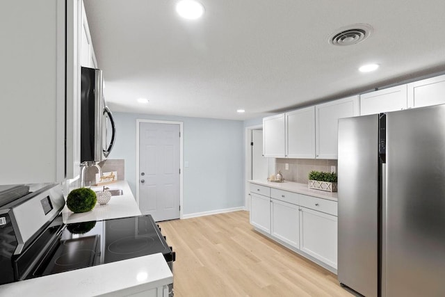 kitchen with stainless steel appliances, light hardwood / wood-style floors, backsplash, white cabinets, and sink