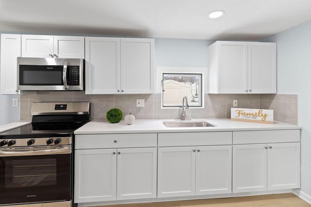 kitchen with sink, white cabinetry, light wood-type flooring, backsplash, and appliances with stainless steel finishes