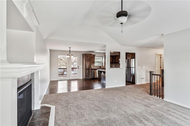 unfurnished living room featuring ceiling fan with notable chandelier, dark carpet, and lofted ceiling