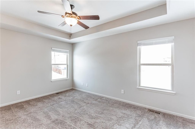 carpeted empty room with ceiling fan and a tray ceiling