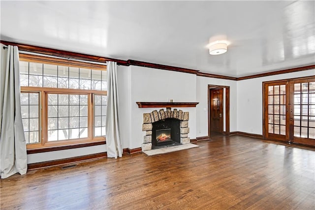 unfurnished living room with hardwood / wood-style flooring, a stone fireplace, a healthy amount of sunlight, and french doors