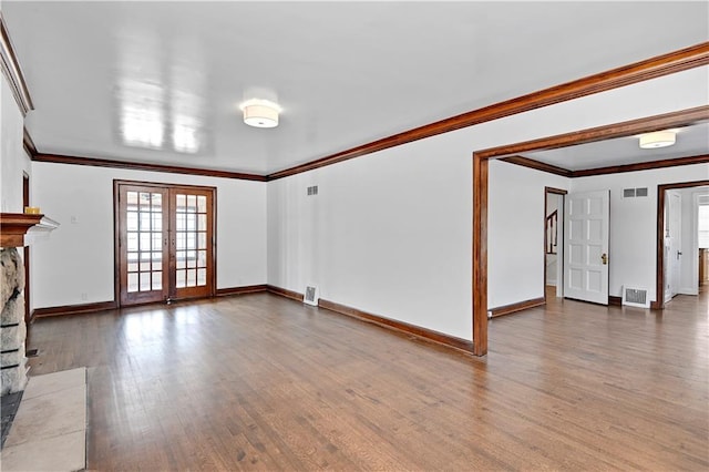 unfurnished living room with a stone fireplace, wood-type flooring, ornamental molding, and french doors